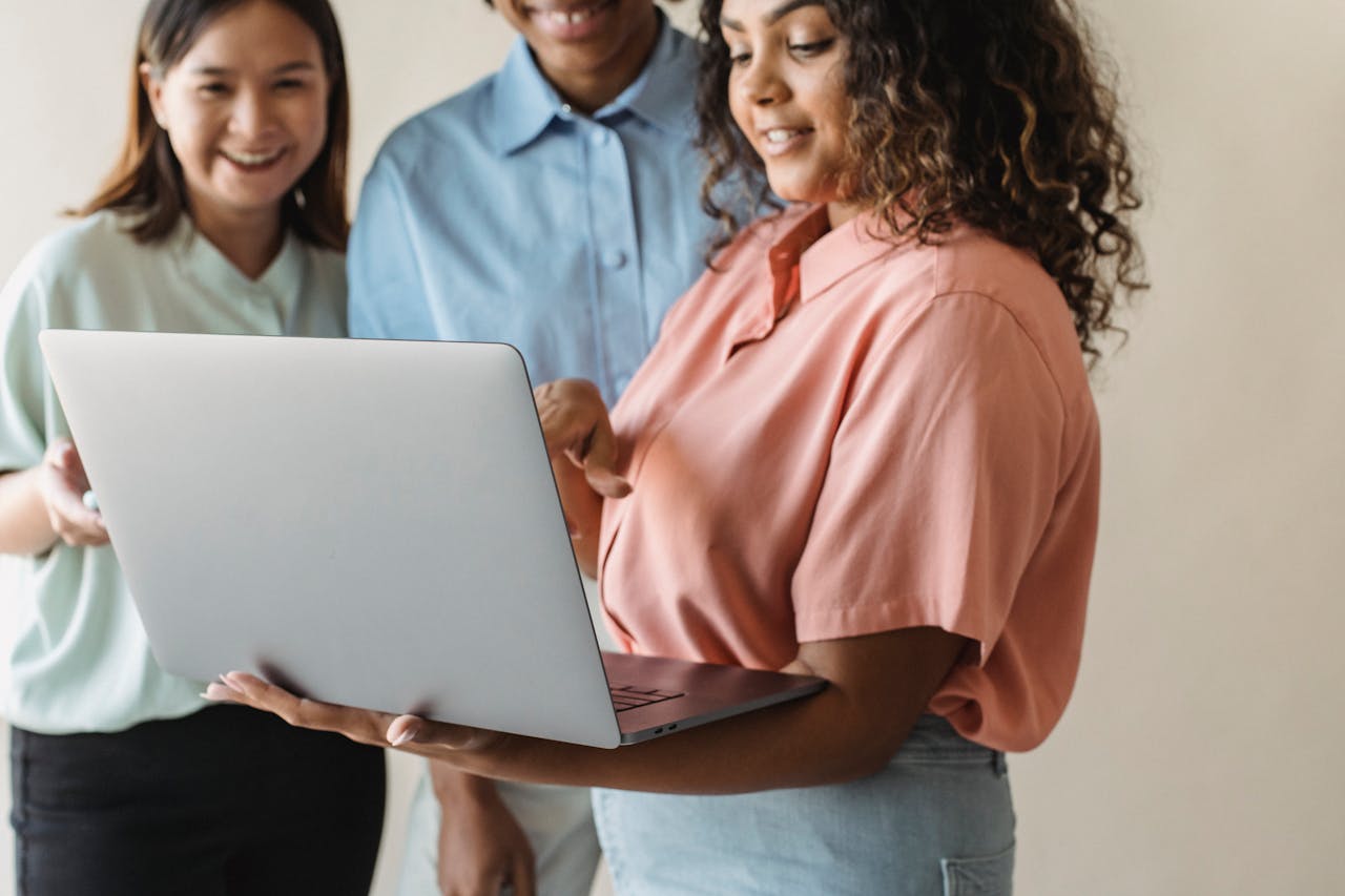 Three diverse women engaging in teamwork on a laptop indoors.